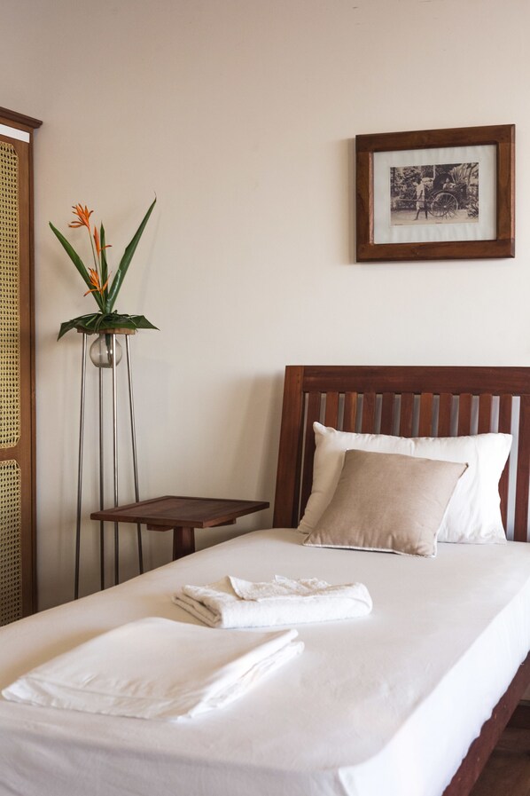 A neatly made bed with white linens, a bedside table, a potted plant, and a framed photograph on the wall.