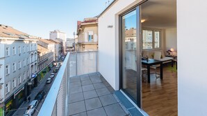 A balcony with a view of a city street, a dining area with a table and chairs, and a sliding glass door leading to an interior space.