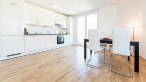 A modern kitchen with white cabinets, a built-in oven, and a dining area with white chairs and a table.
