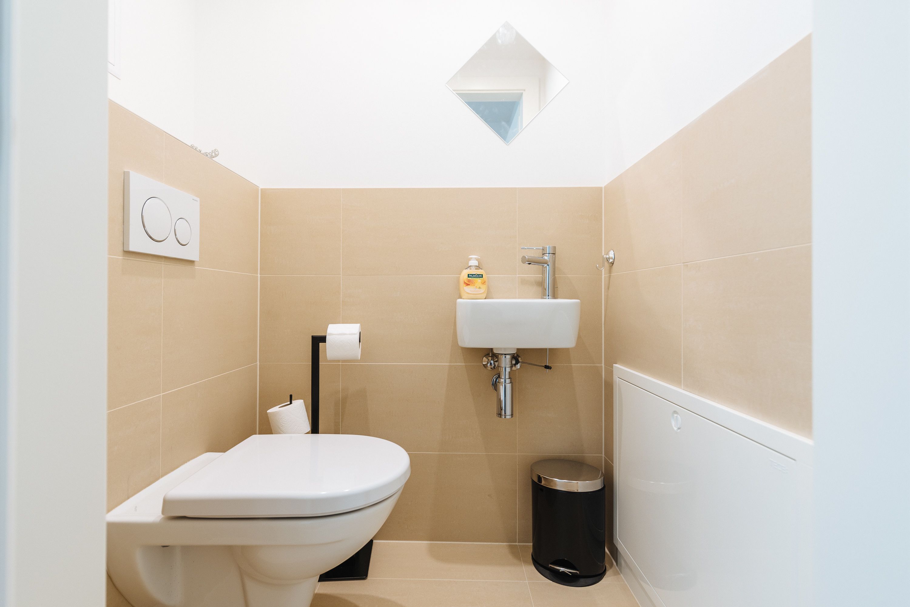 A small, modern bathroom with a toilet, sink, and trash can.