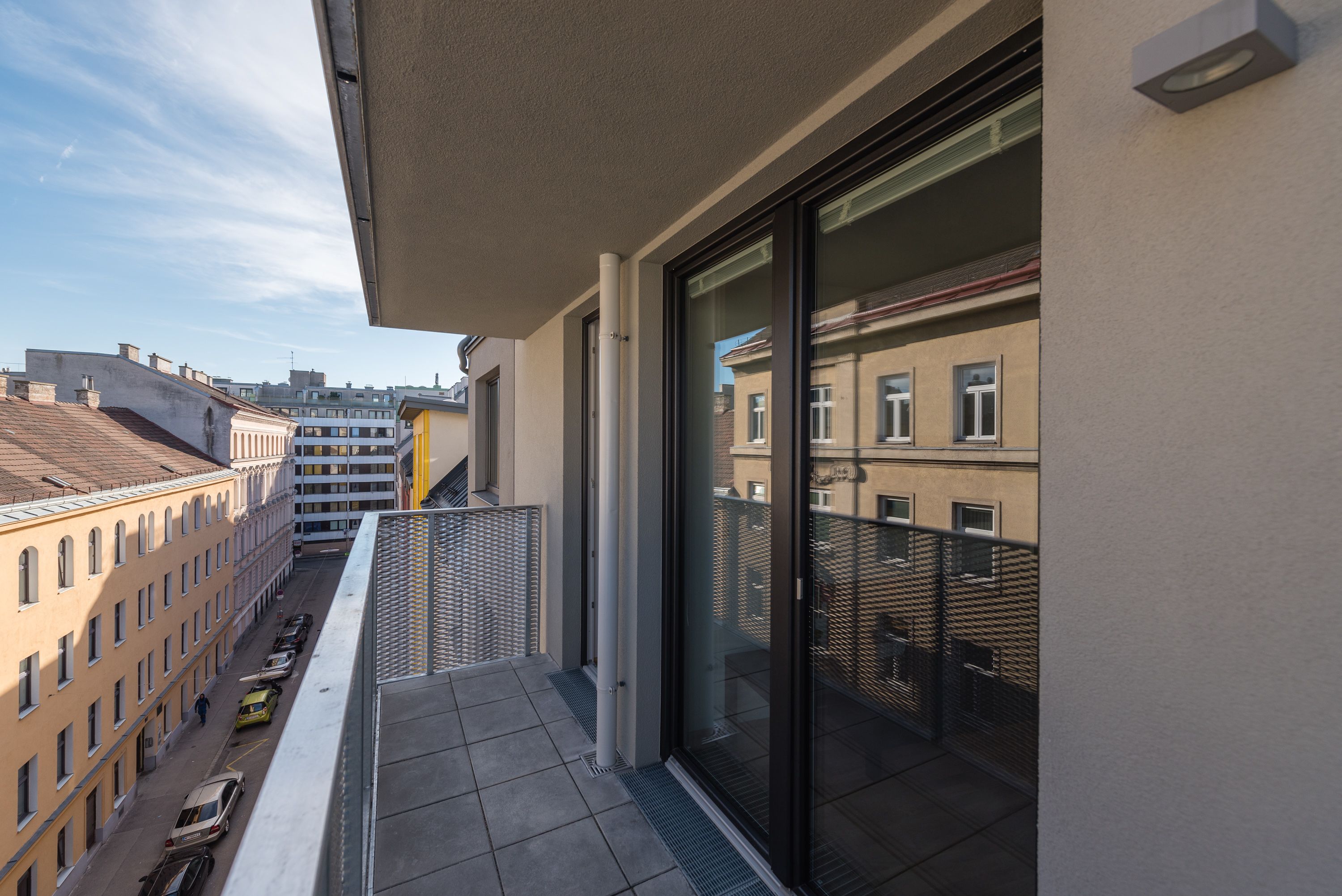 Un balcón con vista a una calle de la ciudad, una puerta de cristal y una barandilla de metal.