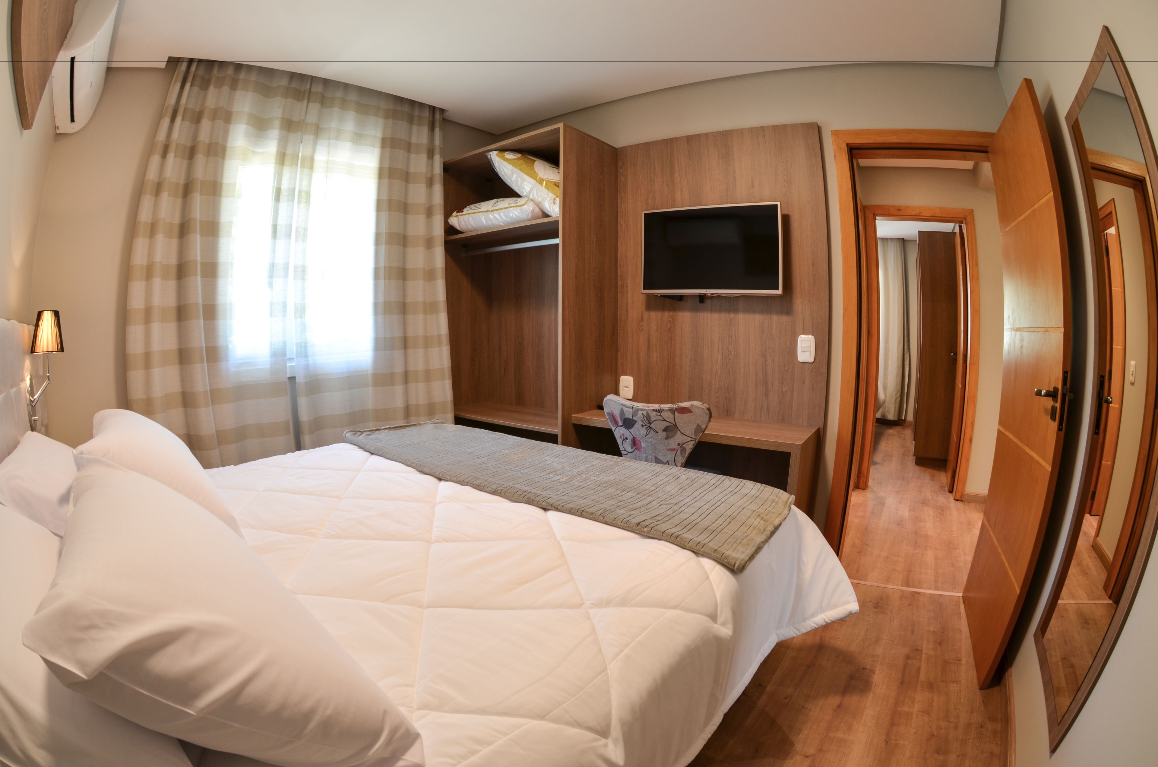 Habitación de hotel con una cama grande, un escritorio con silla, un televisor montado en la pared y un armario.