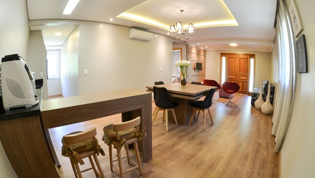A modern kitchen with a wooden countertop, a dining area with a table and chairs, and a hallway leading to a bedroom. - Viena Flats (Gramado)