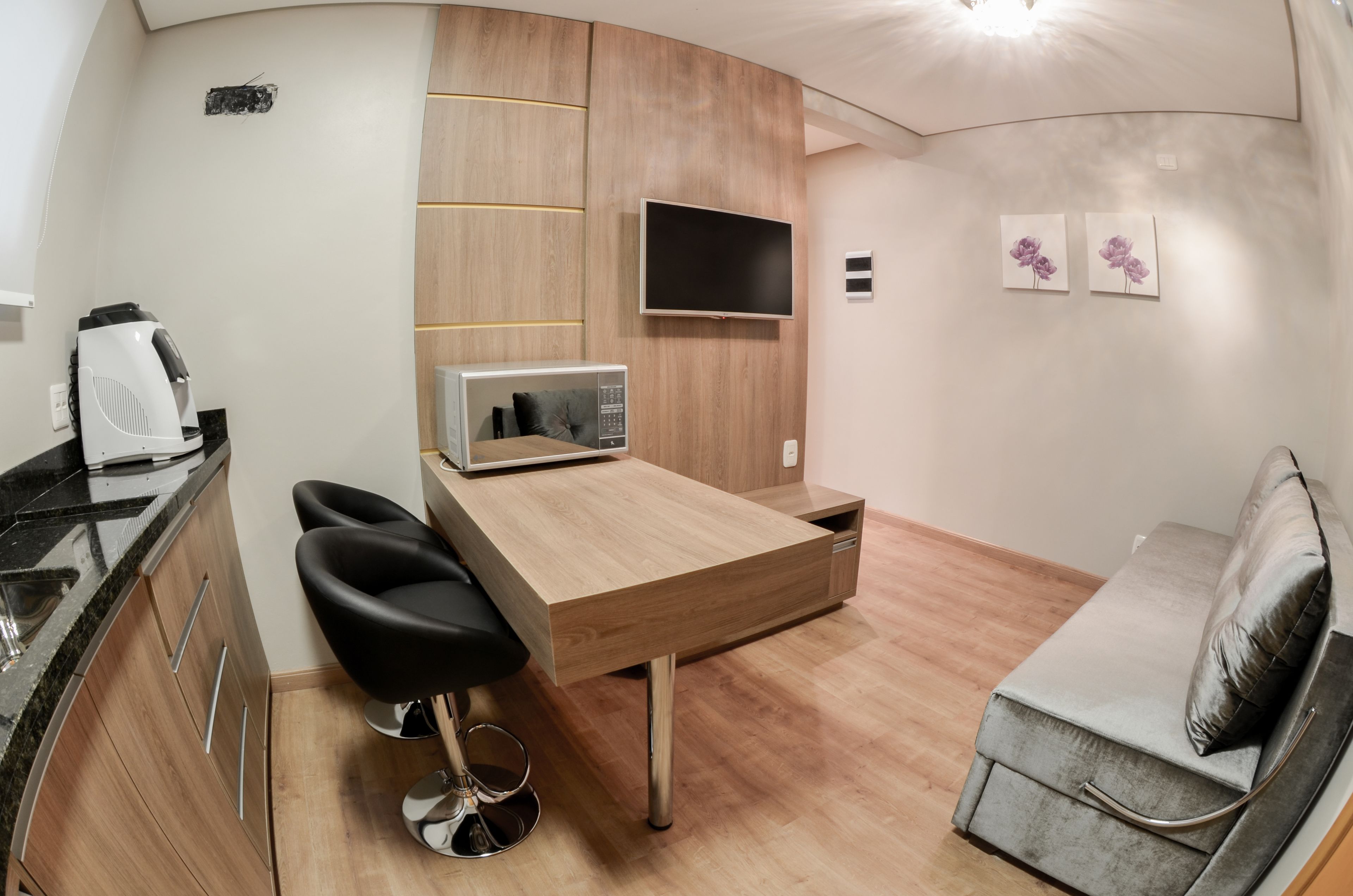 A compact kitchenette with a microwave, coffee maker, and two black bar stools.