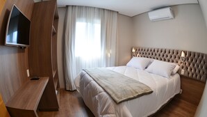 A modern hotel room with a large bed, a TV mounted on the wall, a desk, and a window with curtains. - Viena Flats (Gramado)