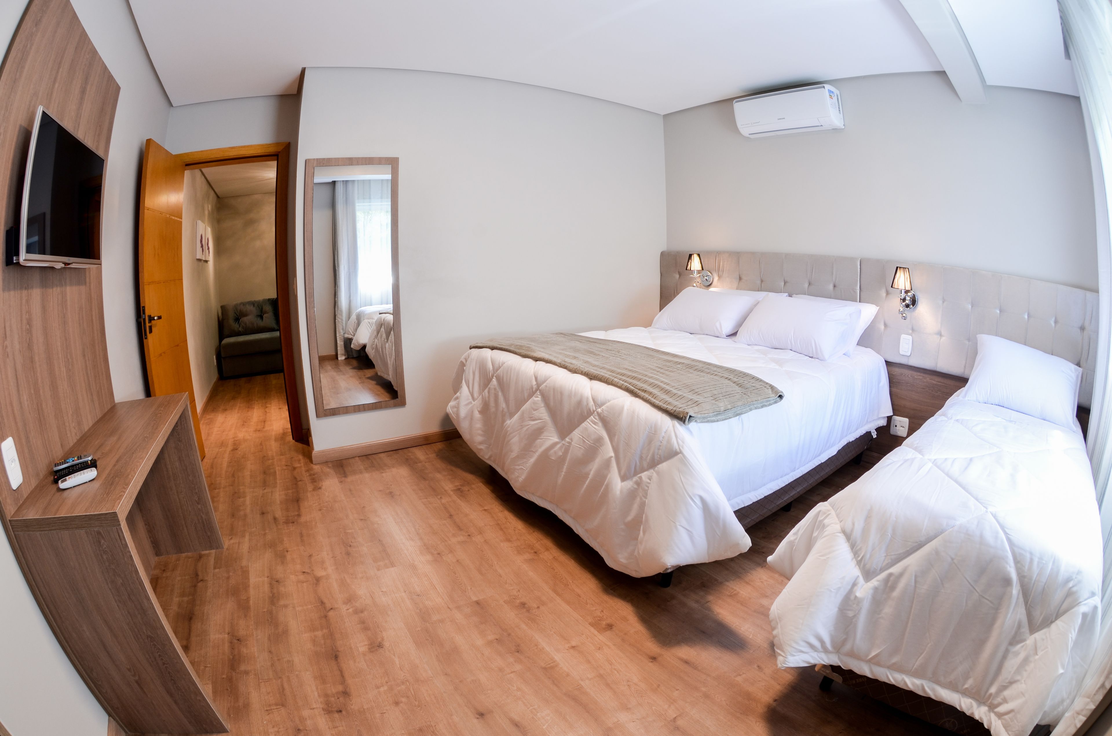 Una habitación de hotel con una cama, mesitas de noche, un televisor y un espejo.