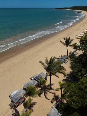 A beach with rows of thatched umbrellas and palm trees, suggesting a resort setting. - Villas de Gaia Hotel Boutique (Porto Seguro)