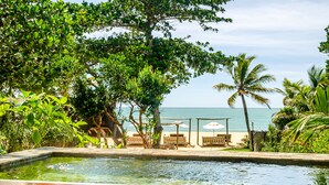 Zona de piscina con cerramiento de vidrio, rodeada de vegetación tropical y vistas al océano.