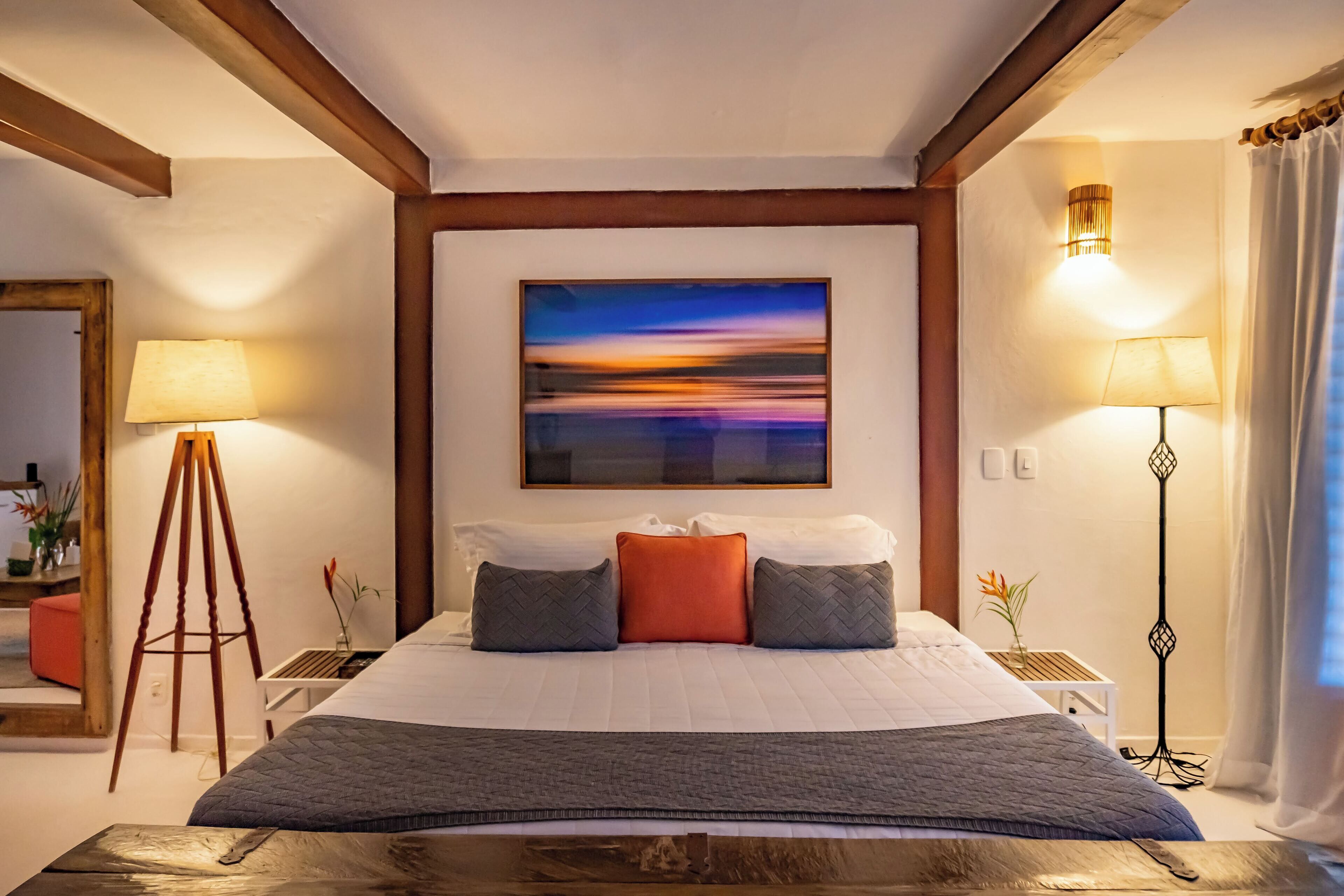 Una camera d'albergo con un letto grande, un quadro appeso al muro e due lampade da comodino.