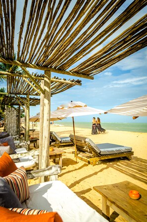 A beachside lounge area with wooden furniture, umbrellas, and a view of the beach and ocean. - Villas de Gaia Hotel Boutique (Porto Seguro)