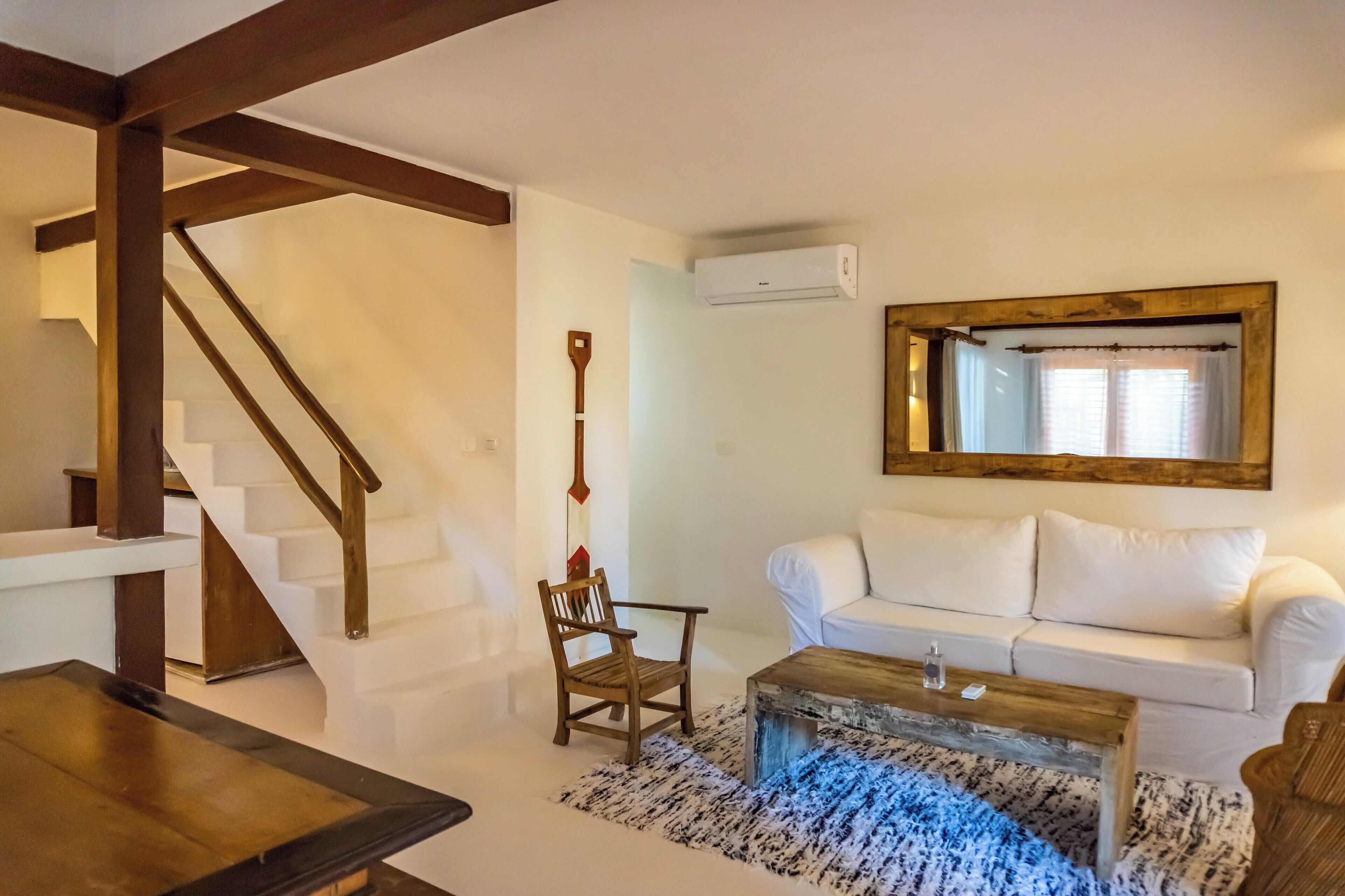 A living room with a white sofa, wooden coffee table, and a staircase with wooden beams.