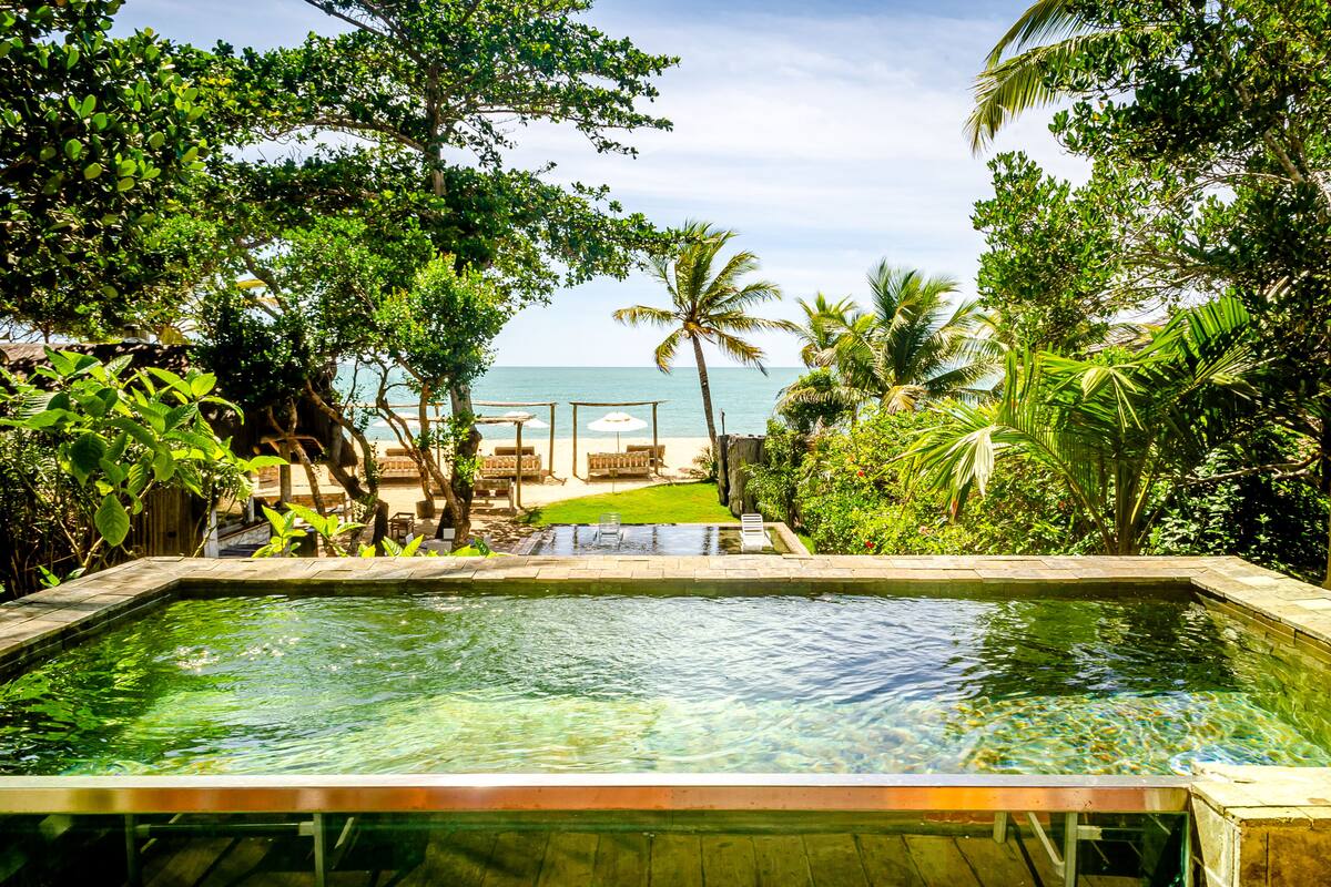 Una piscina con vista sull'oceano, circondata da vegetazione lussureggiante e palme.