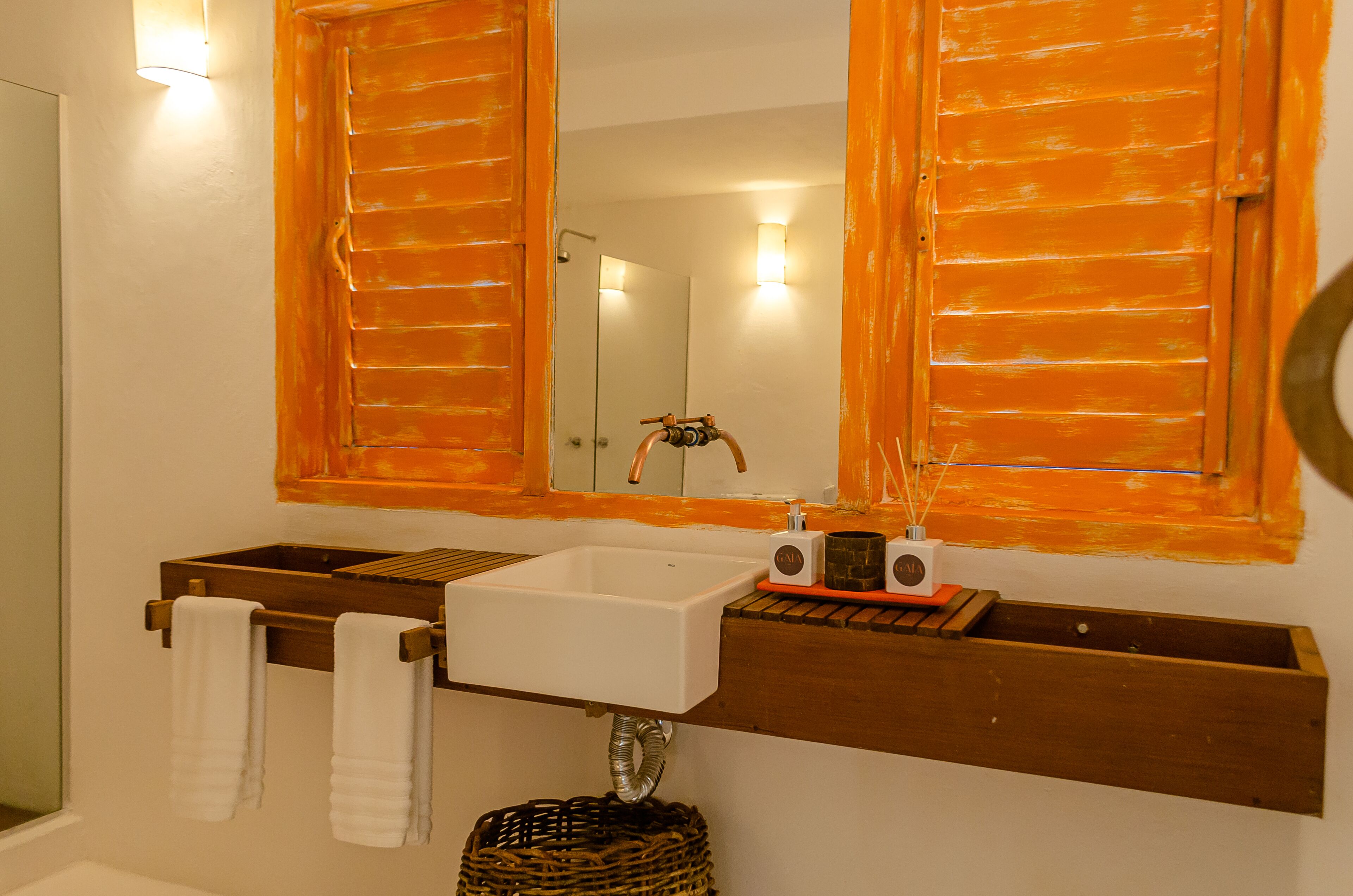 A bathroom with a white sink, wooden towel rack, and two mirrors with orange frames.