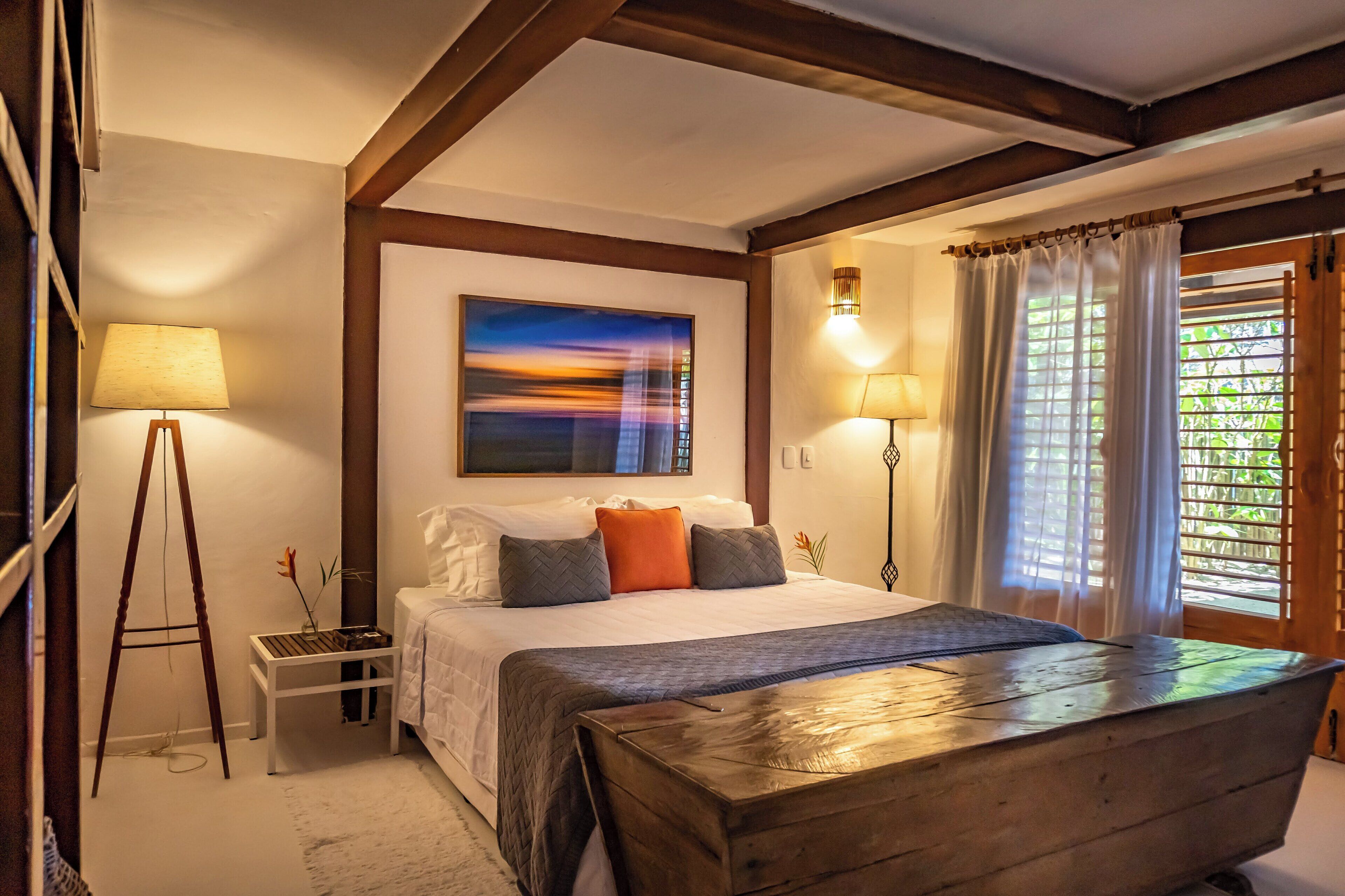 Un dormitorio con cama, lámparas de noche, un cuadro y una ventana con cortinas.