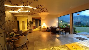 Una sala de estar moderna con un amplio ventanal que da a un espacio exterior, un techo con diseños inspirados en hojas y un conjunto de sofás.
