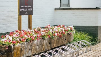 Zona de estacionamiento reservada para bicicletas con un letrero, una jardinera de concreto con flores y un aparcamiento metálico para bicicletas.