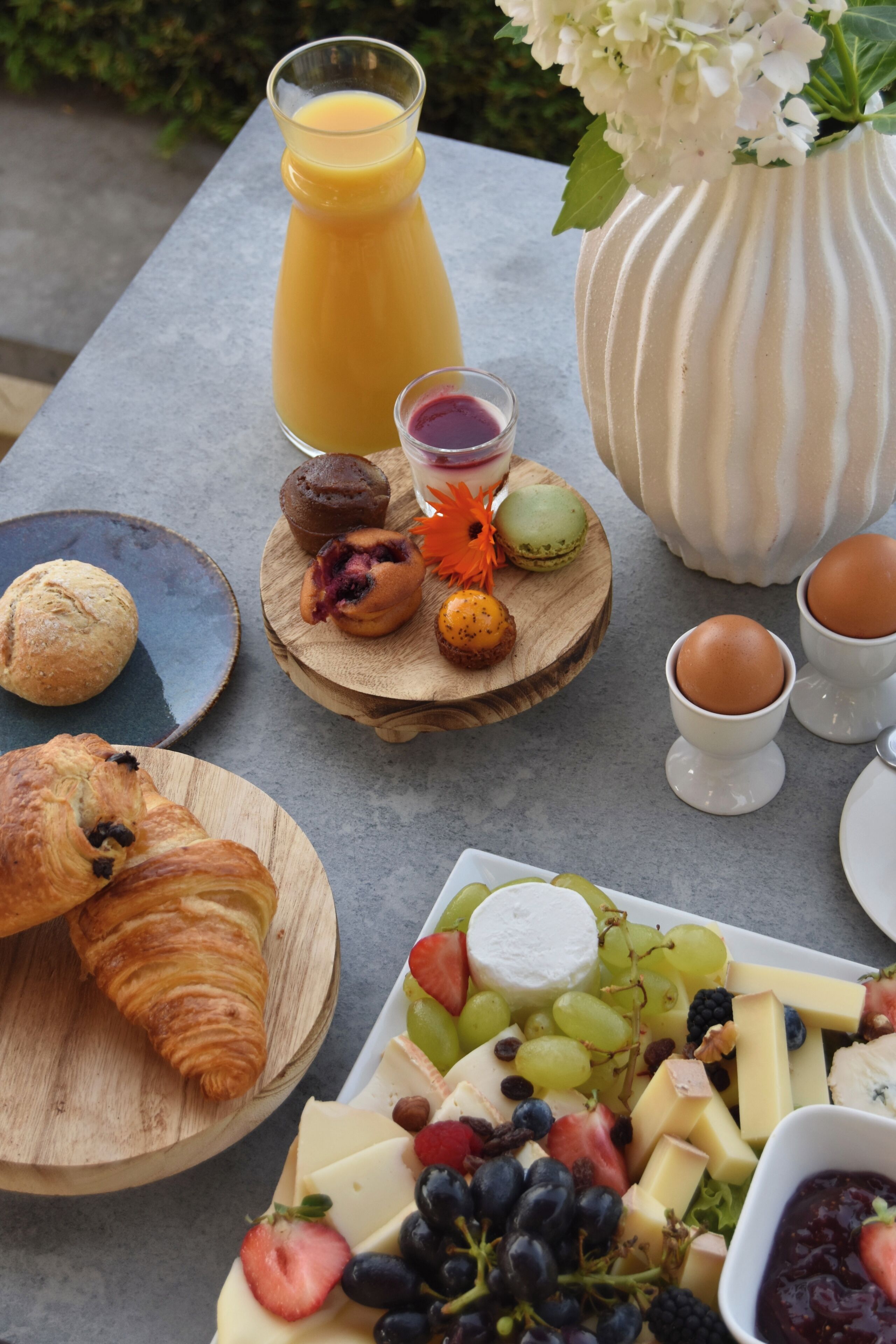 A breakfast table with croissants, pastries, cheese, grapes, strawberries, and a glass of orange juice.