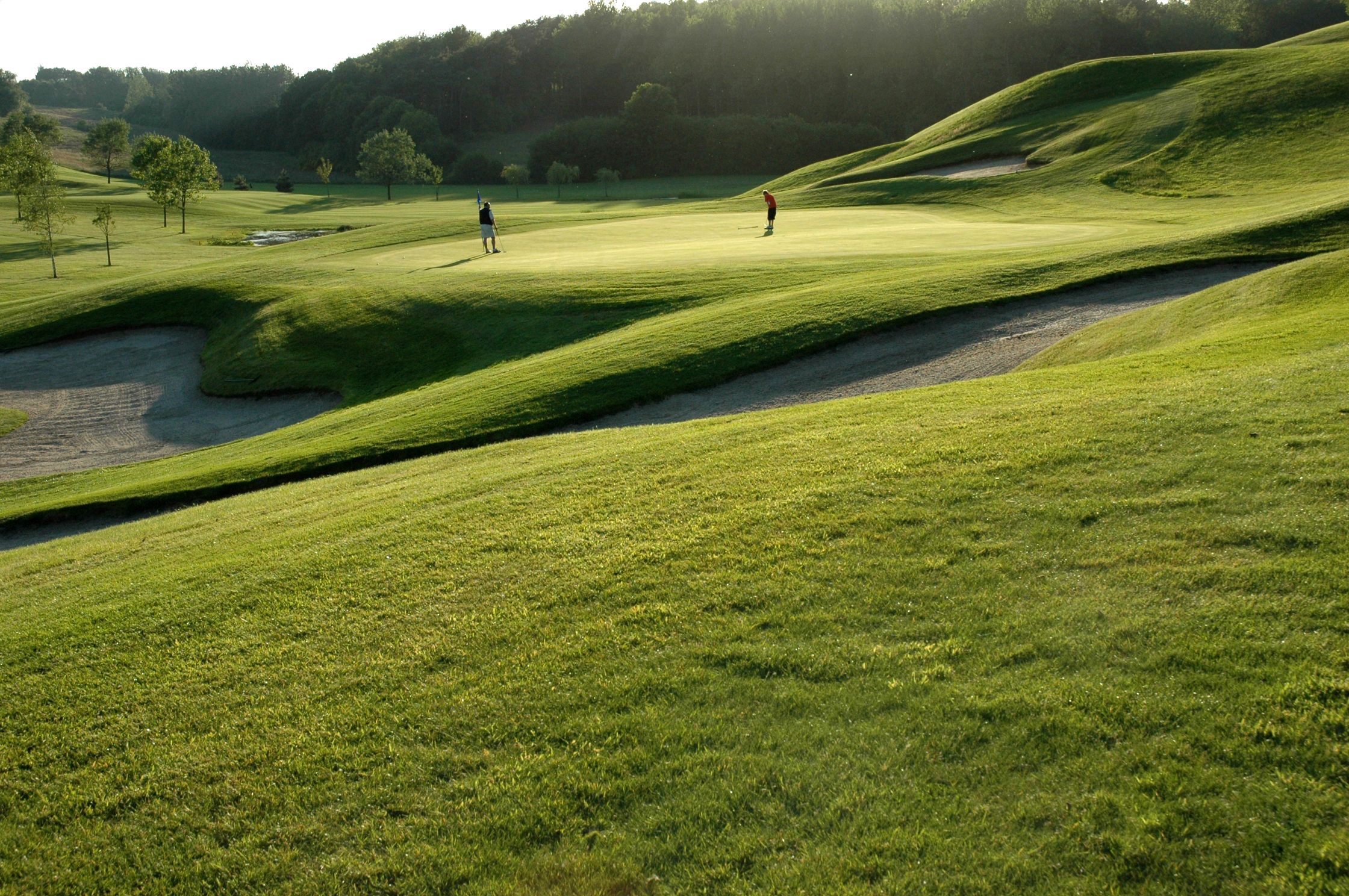 Een golfbaan met glooiende heuvels, zandbunkers en enkele spelers.