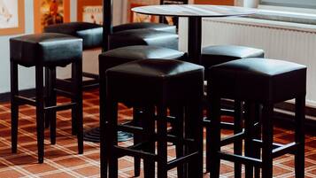 Ein Restaurantinnenraum mit kariertem Boden, schwarzen Barhocker, einem zentralen Tisch und gerahmten Kunstwerken an den Wänden.