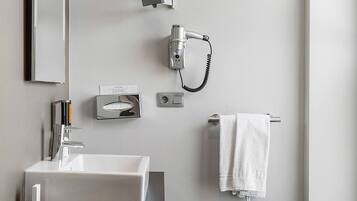 A modern bathroom with a white sink, a mirror, a hairdryer, and a towel rack.