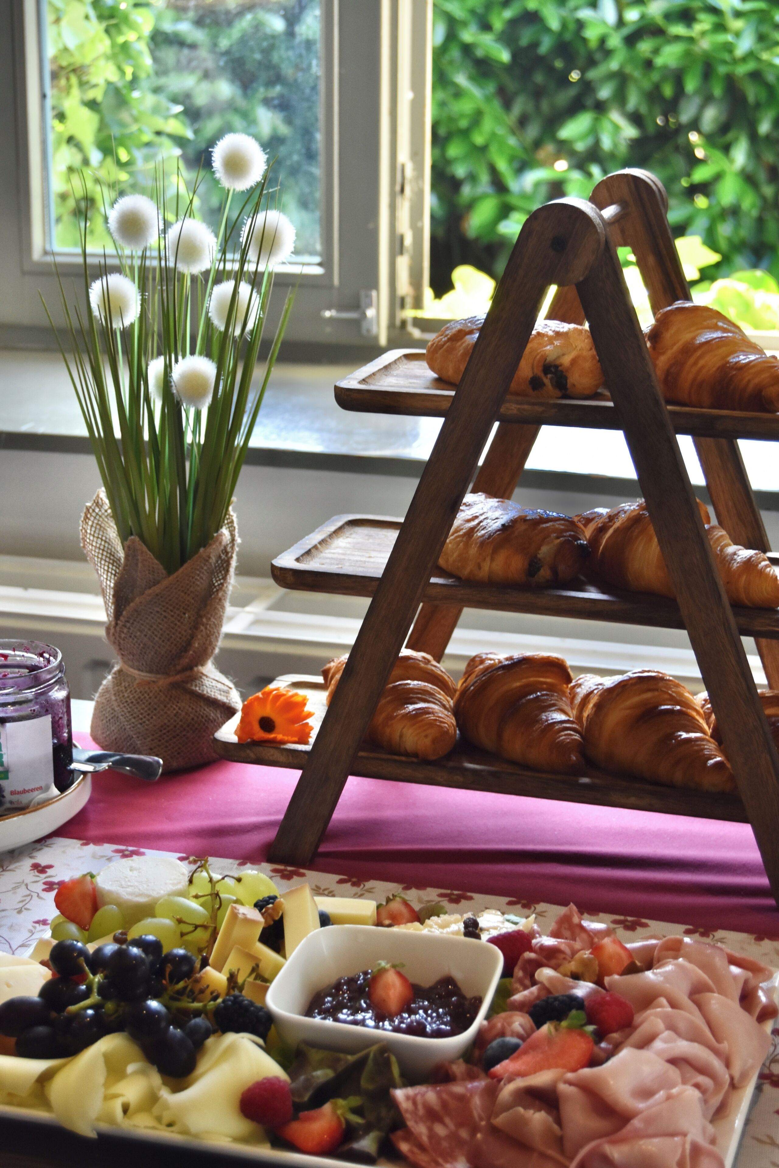 A breakfast buffet with croissants, cheese, fruits, and a vase of flowers.