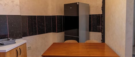 Una cocina con mesa de madera, dos sillas, una lámpara de araña, un refrigerador y salpicadero de azulejos.