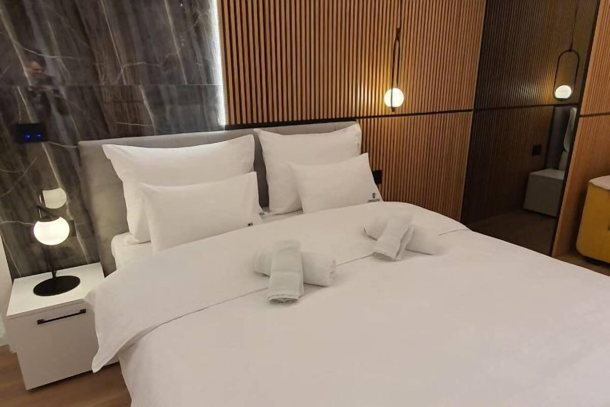 A hotel room with a bed, bedside lamps, a nightstand, and a wooden panel wall.