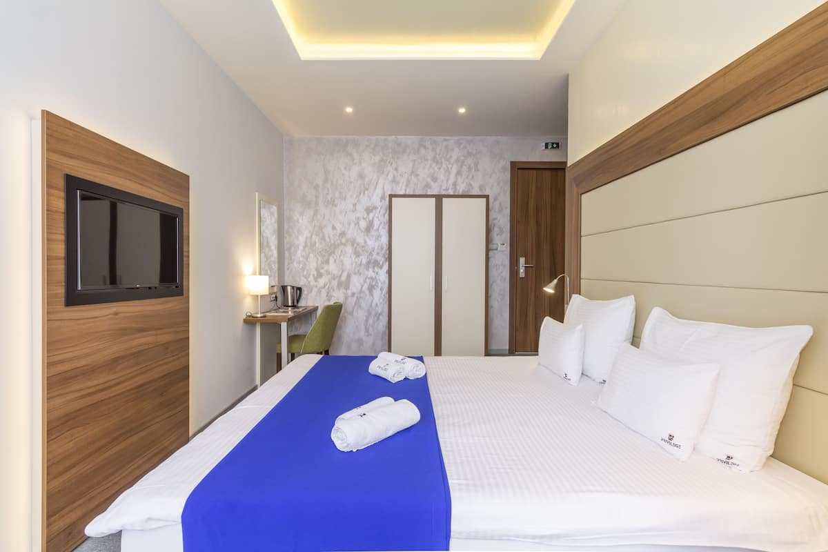 A hotel room with a bed, a television mounted on the wall, a desk with a chair, and a door.