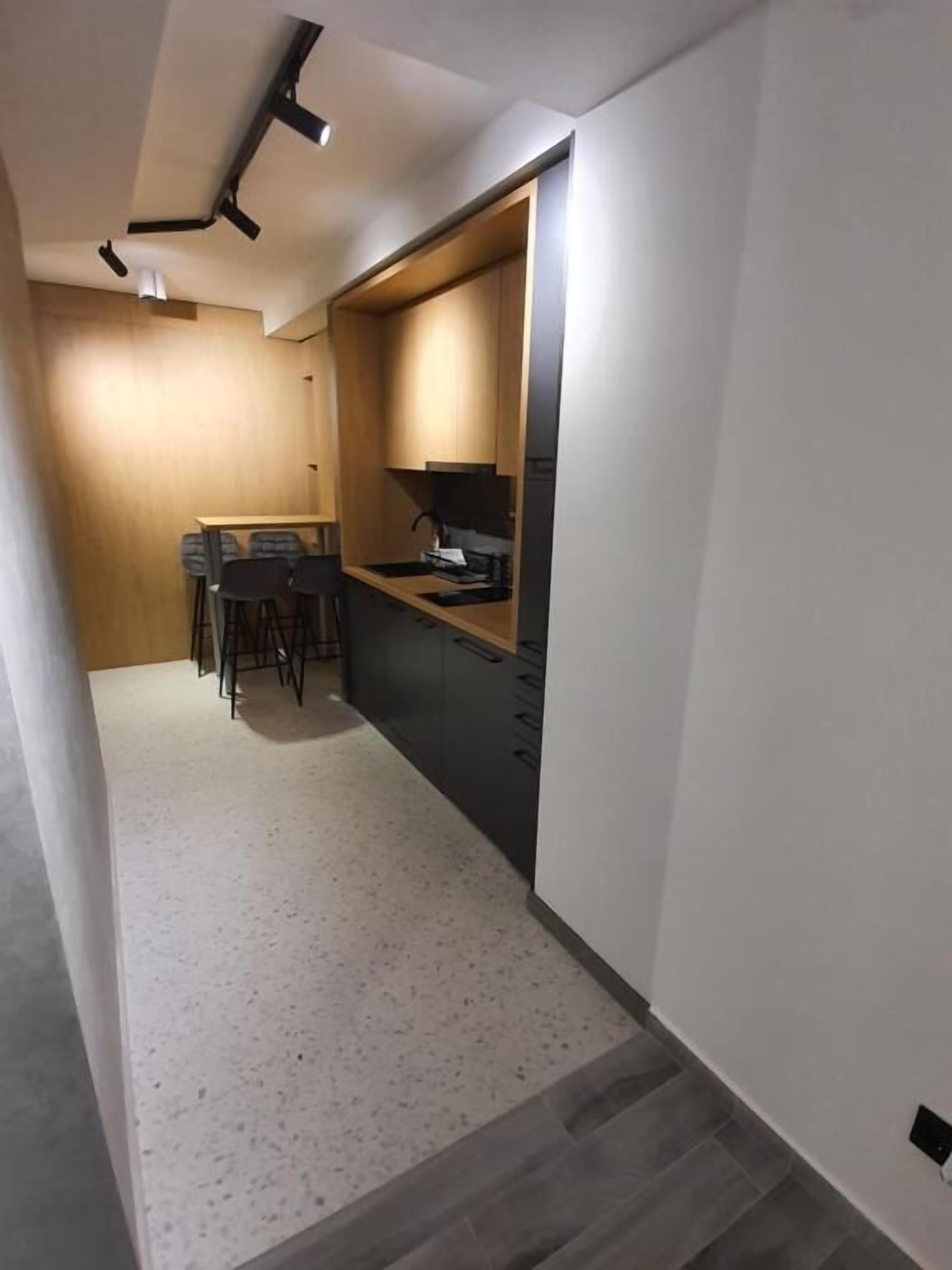 Una cocina moderna con armarios oscuros, una zona de comedor con mesa y sillas, y un pasillo con piso de colores claros.