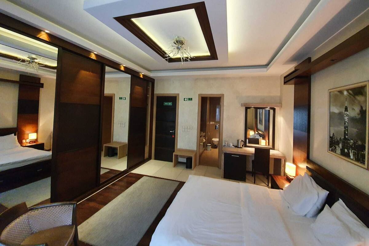 A hotel room with a large bed, a desk, a chair, a mirror, and a ceiling light fixture.