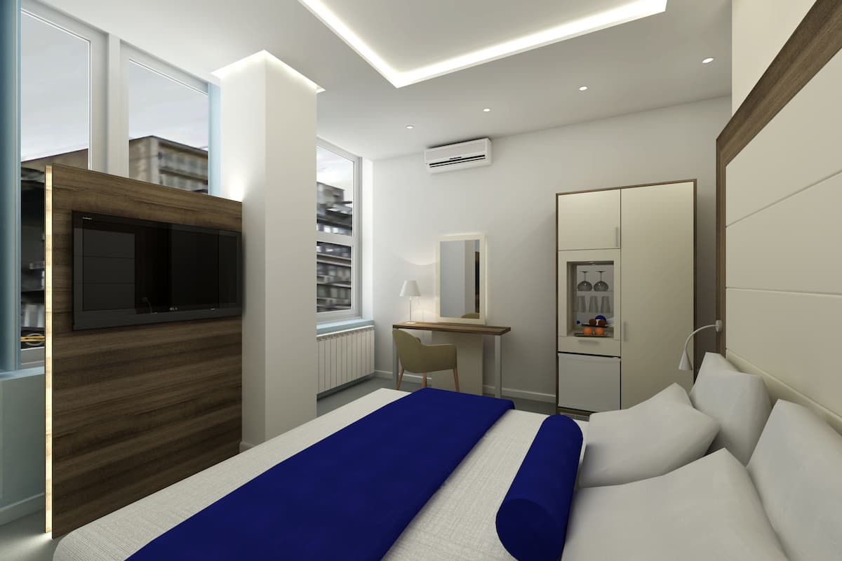 A modern bedroom with a large bed, a TV mounted on a wooden panel, a desk with a chair, a wardrobe, and a window with a city view.