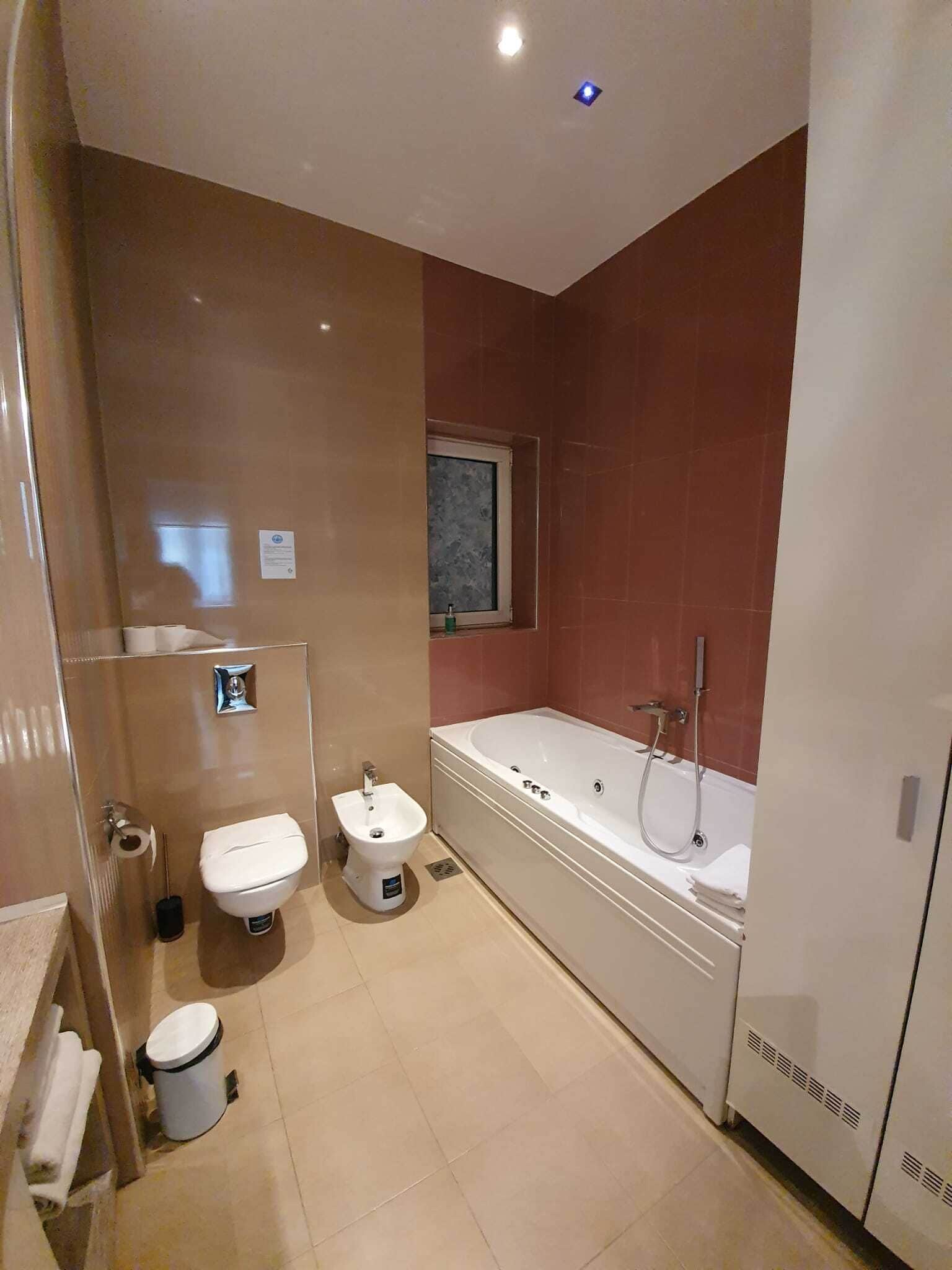 A modern bathroom with a bathtub, toilet, bidet, and a window.