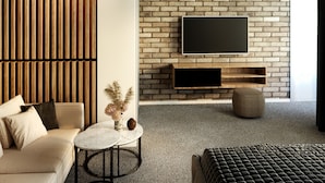 A modern living room with a brick wall, a flat-screen TV, a sofa, a coffee table, and a patterned ottoman.