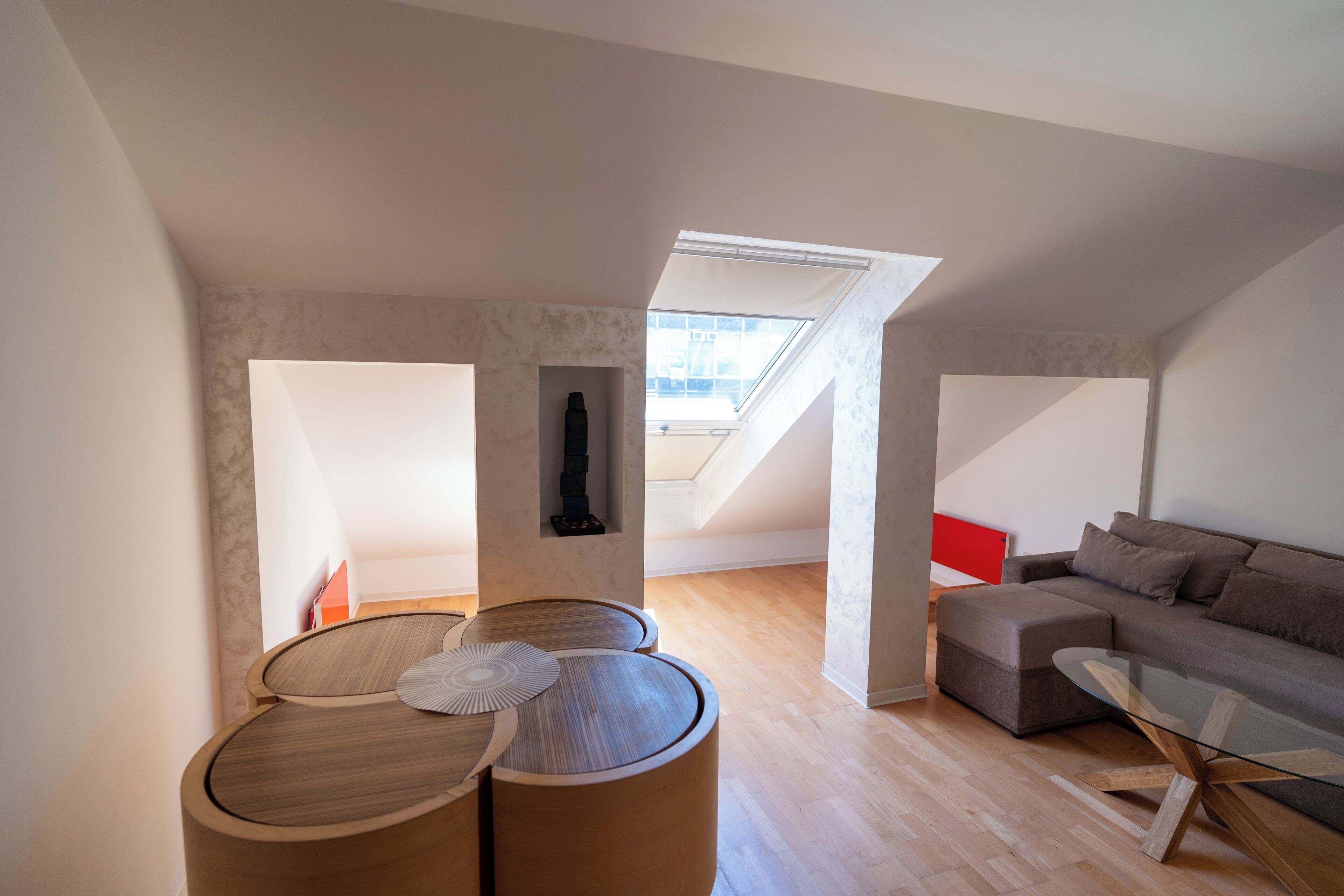 Ein modernes Loft-Apartment mit Dachfenster, einem Glastisch, einer Couch und einem kleinen Holztisch.