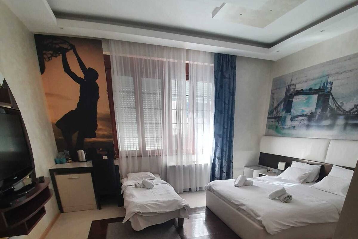 A hotel room with two beds, a desk, a television, and a painting of a bridge.