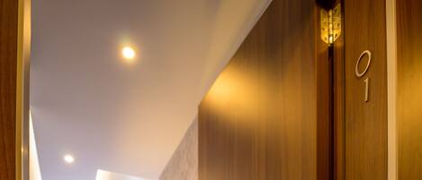 A hallway with a wooden door marked with the number 1, leading to a room with a radiator and a window with curtains.