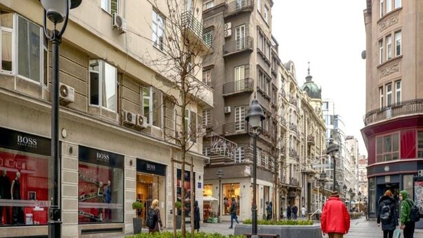 A pedestrian street with shops, benches, and a tree-lined walkway.
