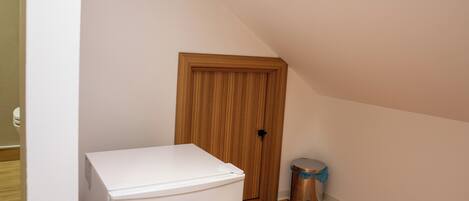 A compact room with a white refrigerator, a wooden door, and a trash bin.