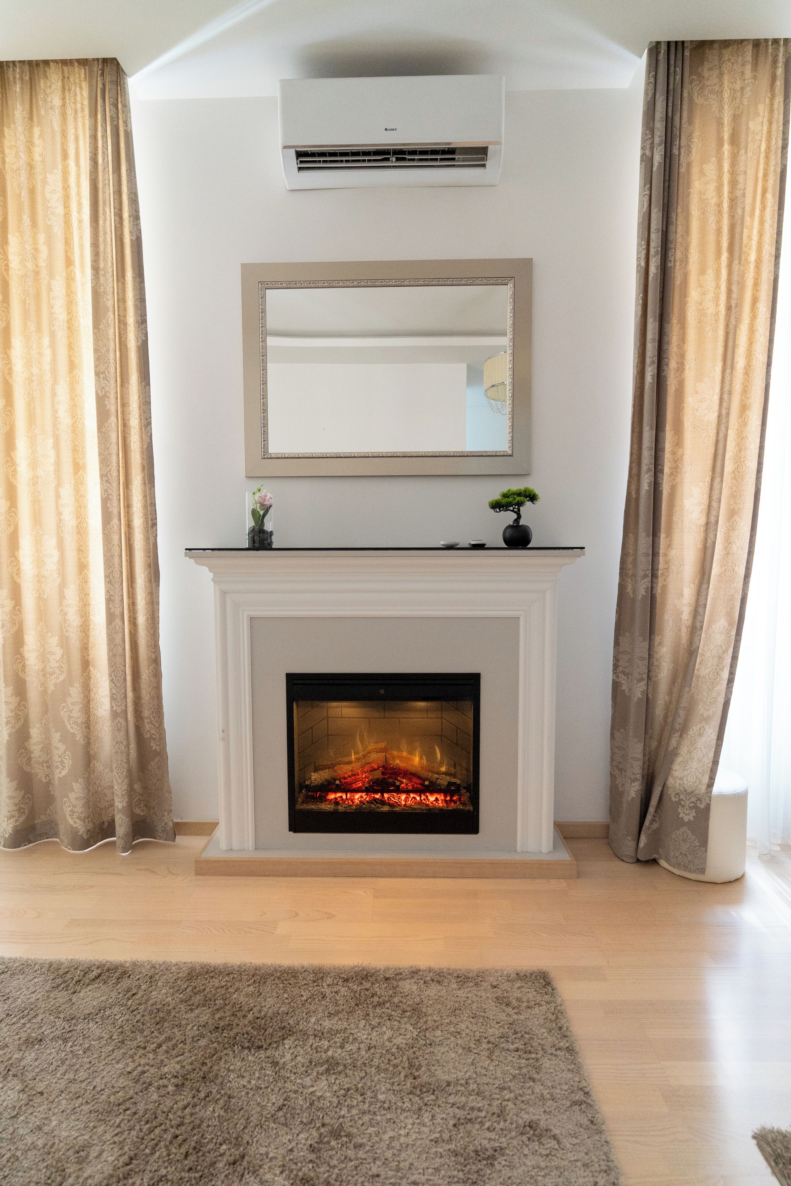 A room with a fireplace, a mounted mirror, and a ceiling-mounted air conditioning unit.