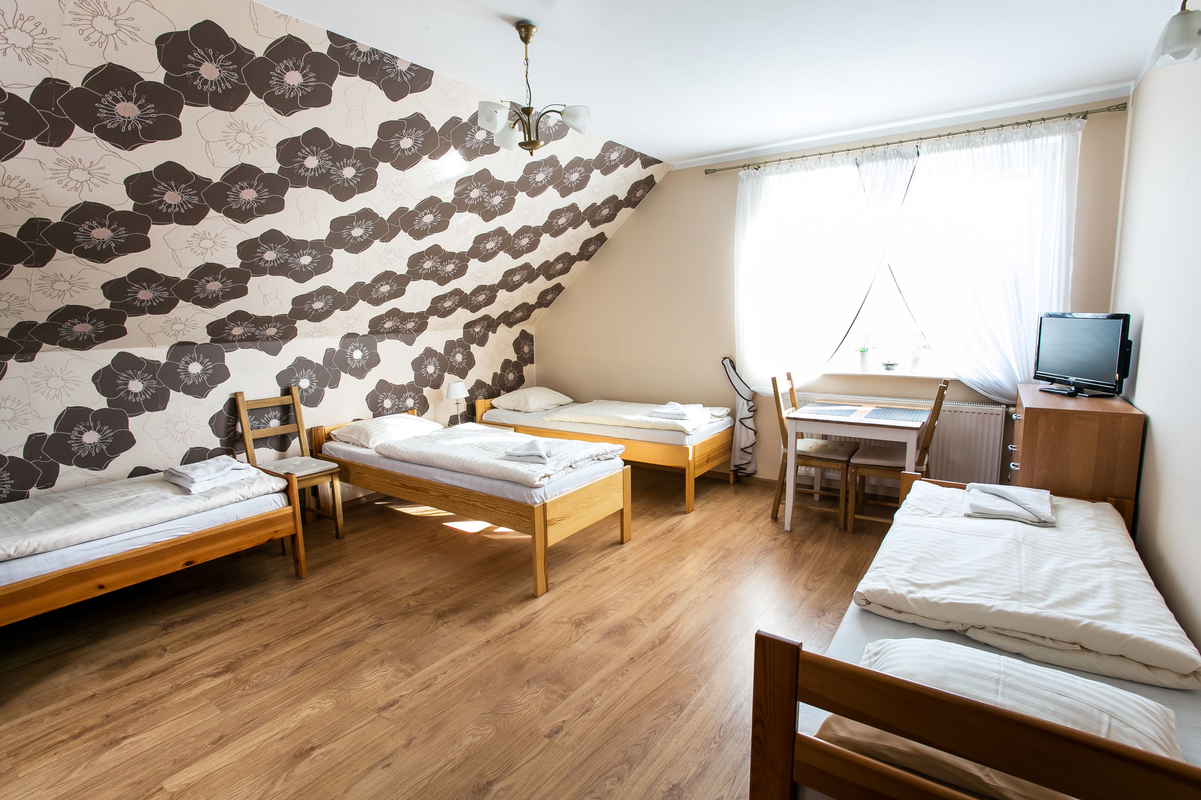 A dormitory room with two single beds, a desk, a chair, and a television.