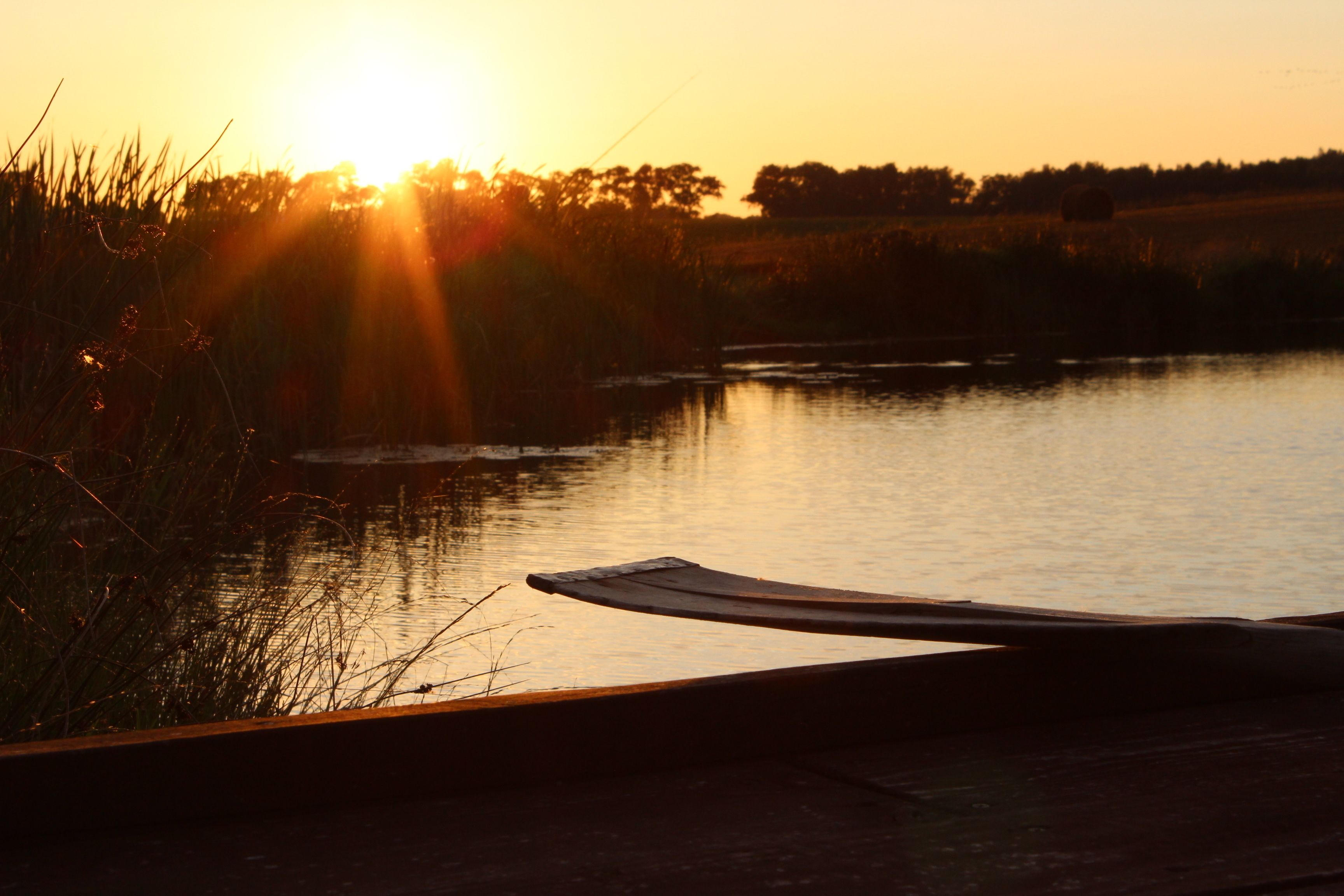 Un coucher de soleil sur une étendue d’eau calme, avec une pagaie au premier plan.