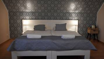 A double bed with a white frame, two bedside tables with lamps, and a patterned wallpaper.
