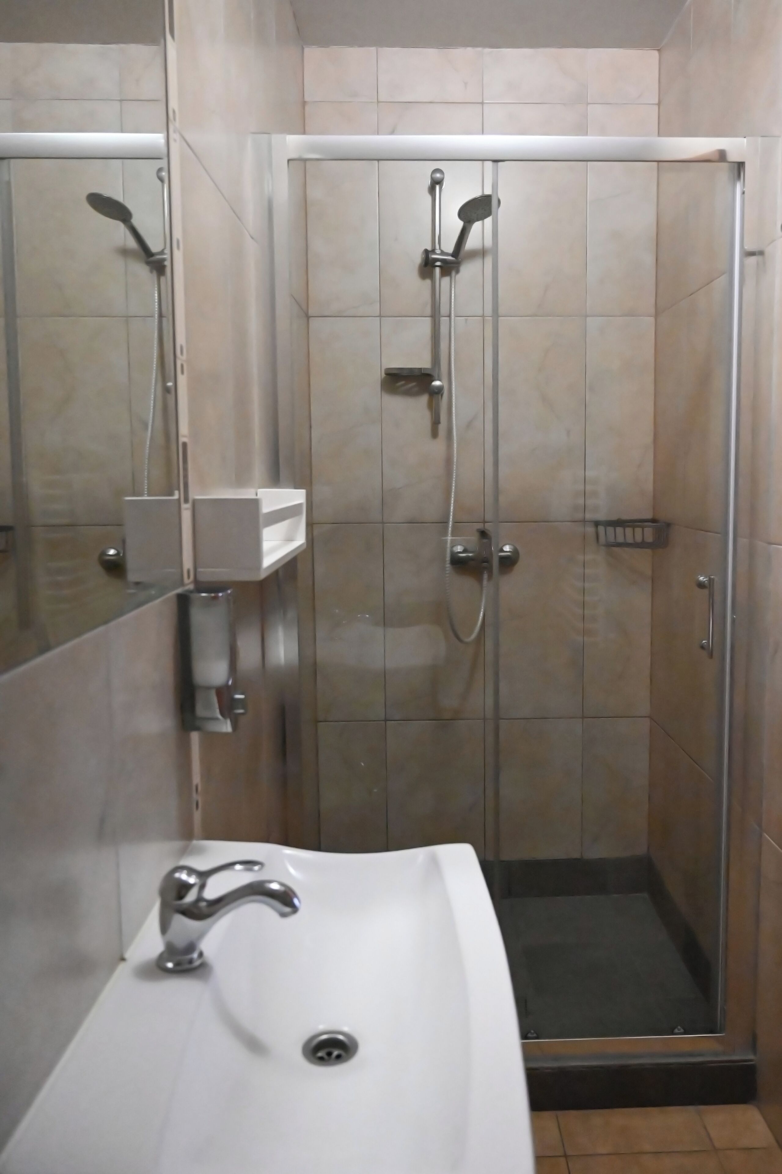 Ein Badezimmer mit einem weißen Waschbecken, einem Spiegel und einer gläsernen Duschkabine.