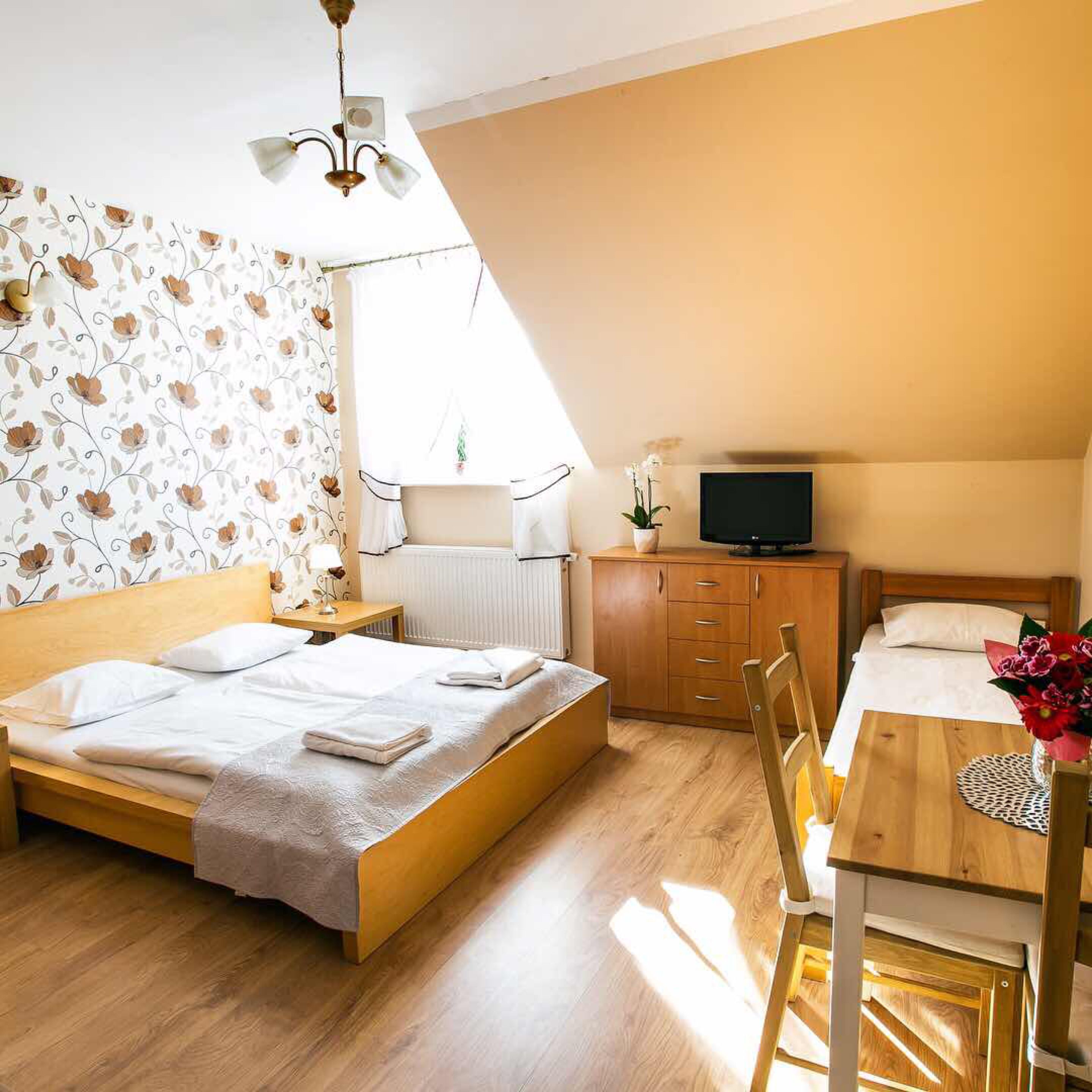 A bedroom with a bed, a desk, a chair, a TV, and a radiator.