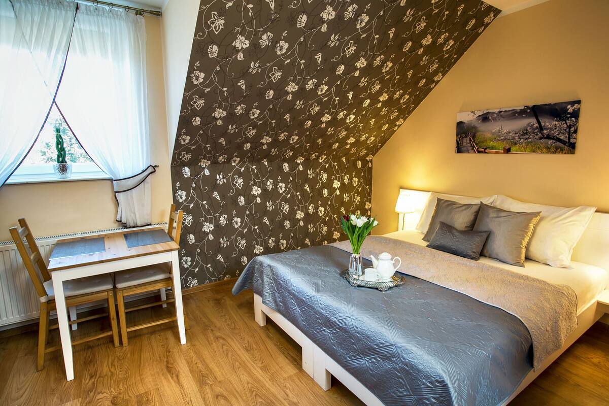 A bedroom with a bed, bedside table, and a window with curtains.