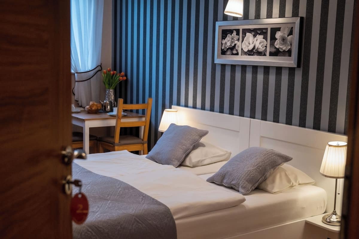 A hotel room with a bed, bedside table, chair, lamp, and a framed floral artwork on the wall.