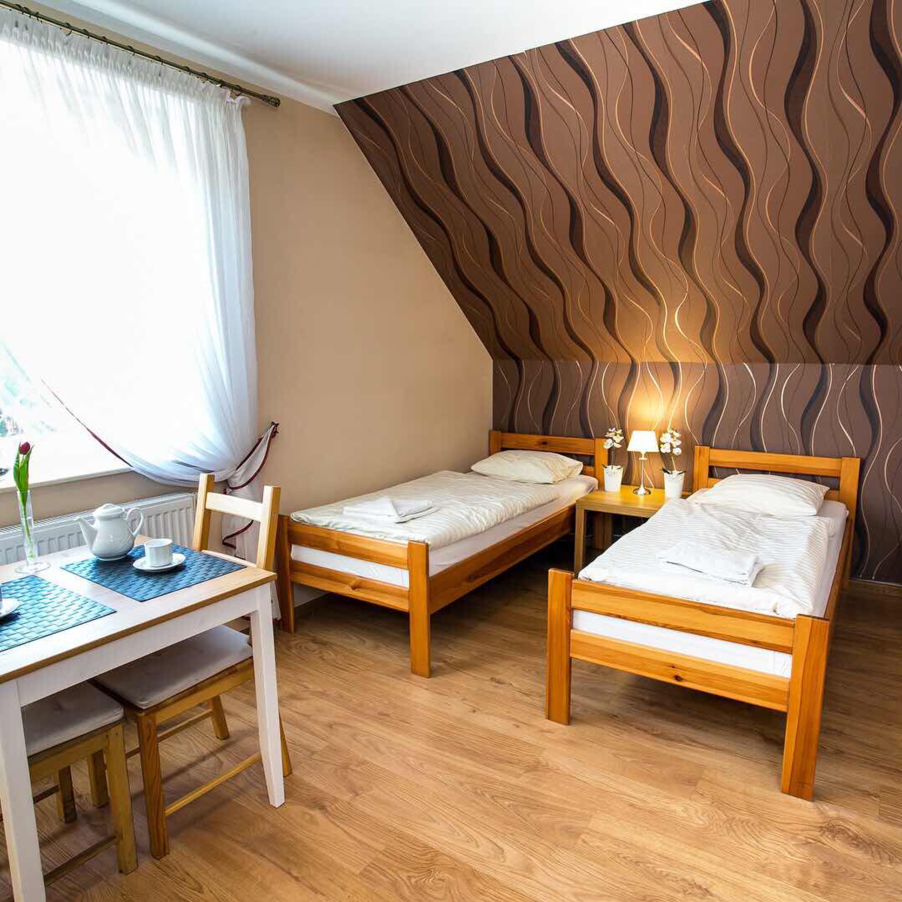 A room with two wooden beds, a table with a chair, and a window with curtains.