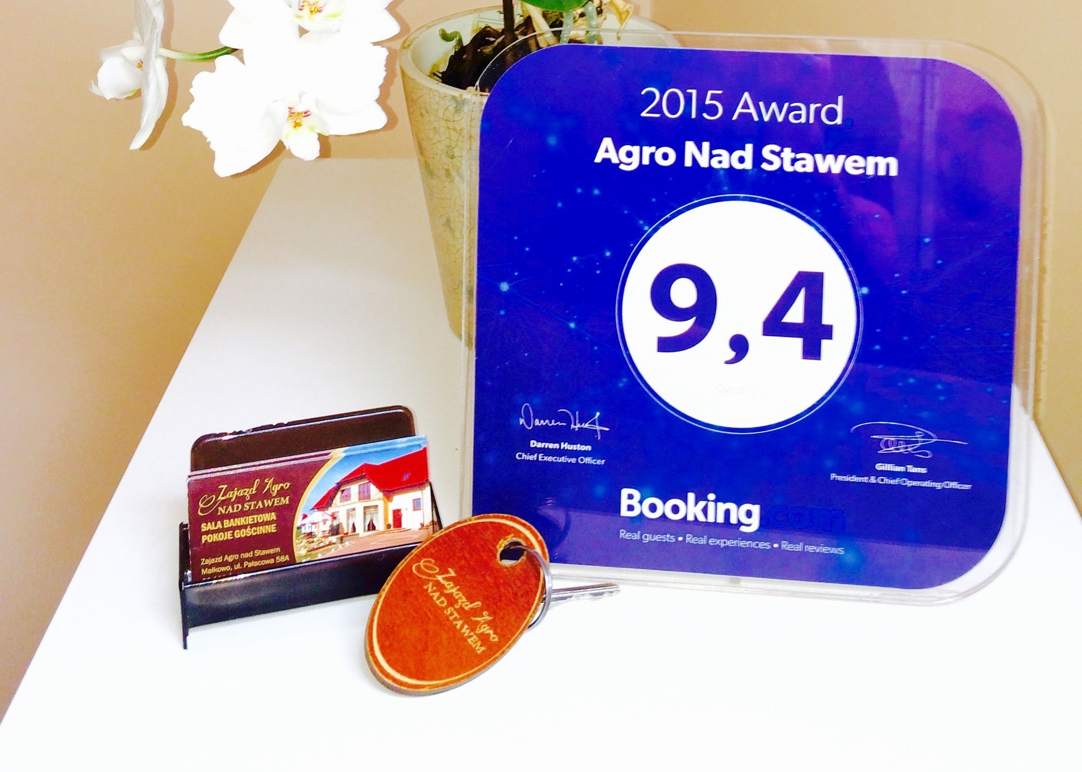 A 2015 Award plaque for Agro Nad Stawem with a score of 9.4, a book titled 'Zajazd Agro nad Stawem', and a tag with the hotel's name.