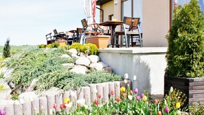 An outdoor seating area with tables and chairs, a stone retaining wall, and a variety of plants and flowers. - Zajazd Agro nad Stawem (Zukowo)