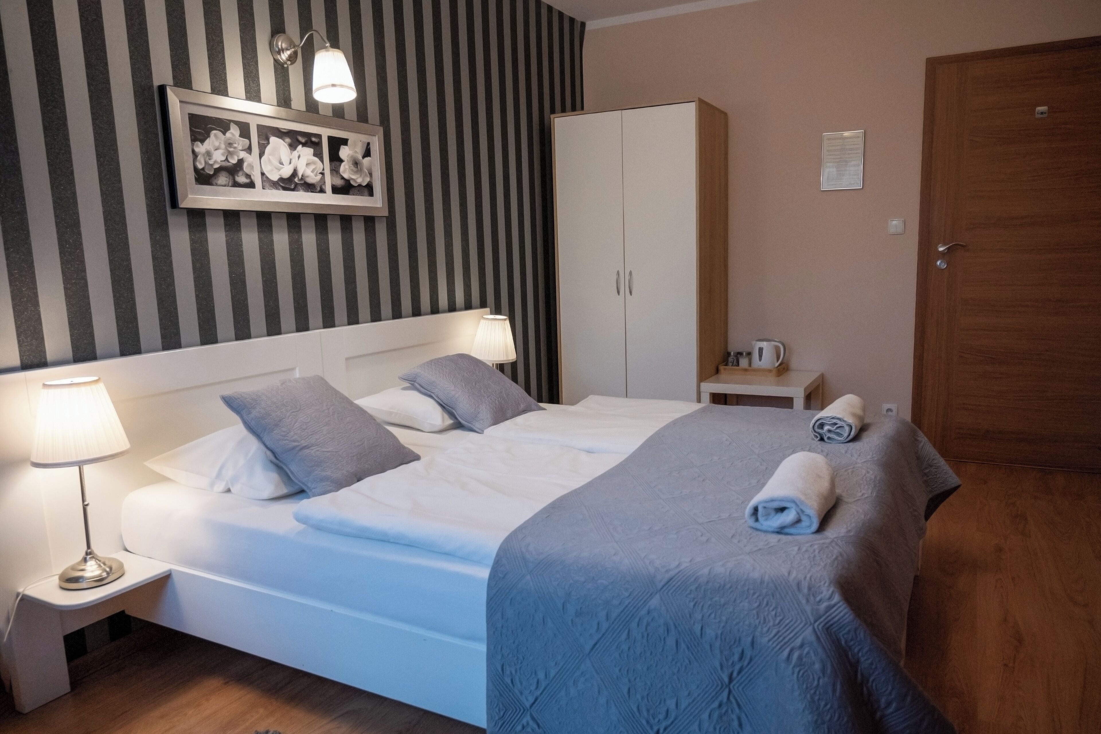 A neatly made bed with pillows, a bedside lamp, a framed picture on the wall, a wardrobe, and a door.